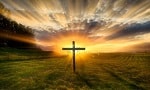 Silhouetted cross at sunset in an open field